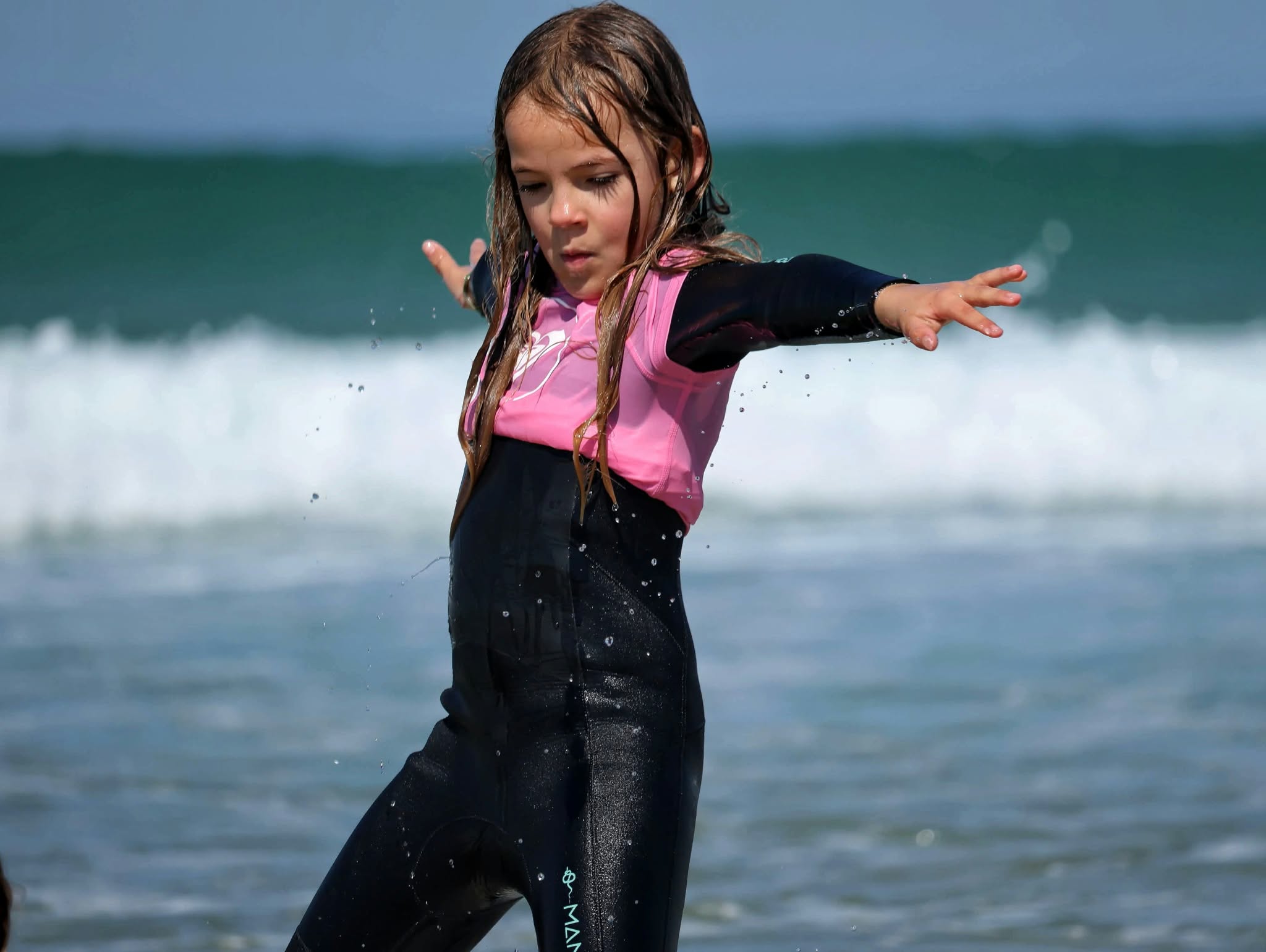 Jeune surfeuse en rose, bras tendus devant les vagues