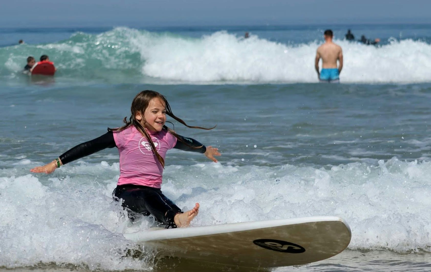 Jeune surfeuse souriante portée par une vague sur sa planche